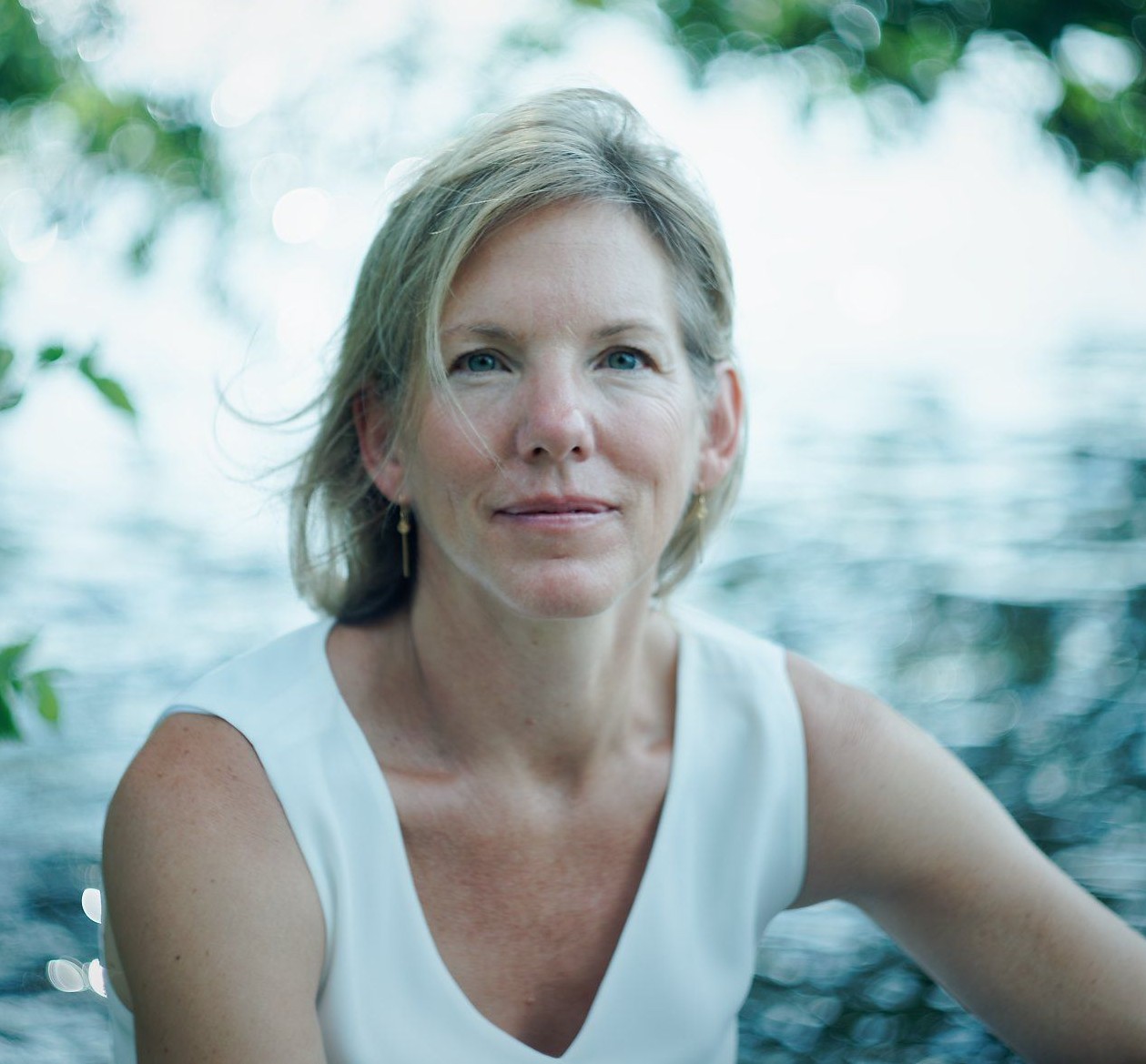 woman with blonde hair wearing white sleeveless shirt under some tree branches 