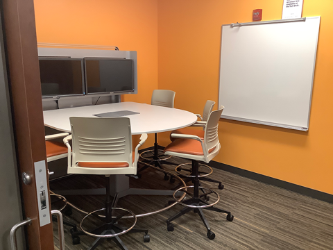 Photo of Study Room 3, with a half-round table and six chairs facing dual monitors, and a white board on the side wall.