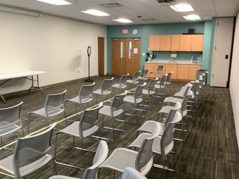 Photo of the north half of the Meeting Room with chairs arranged in rows facing the front wall. A sink and cabinets are adjacent to the entry doors.