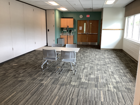 Photo of the south side of the Meeting Room, with one table and four chairs in the middle of the room. A small sink and cabinet is adjacent to the entry doors.