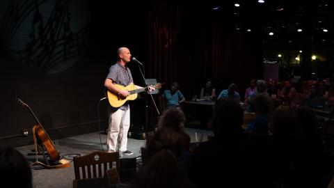 Man on stage playing a guitar facing the audience.