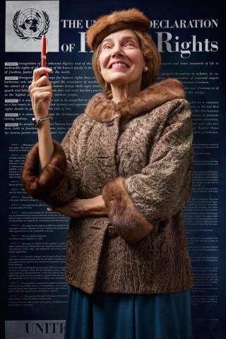 Woman wearing brown fur coat with right arm in air holding a pen against a backdrop of The Declaration of Human Rights