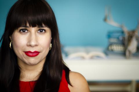 Headshot of brown haired Erika Sanchez in a red dress with a blurred backgrond