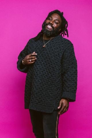 scholar Jason Reynolds an African American male wearing all black, set on a back drop of fuschia