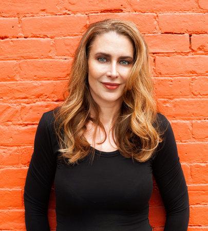 woman with red hair wearing black long-sleeved shirt standing in front of a brick wall