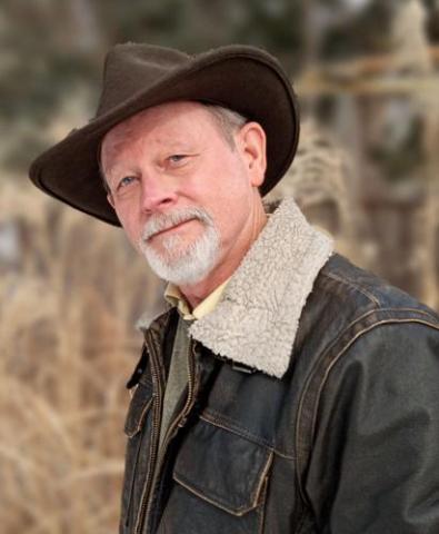 man with grey beard and cowboy hat somewhat smiling at the camera