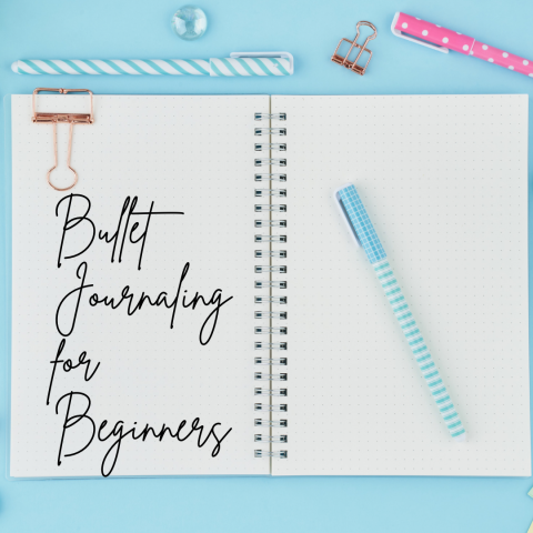 image shows a white notebook on a blue background.  Bullet Journaling for beginners is written across the left page in script and a blue pen sits on the right side 