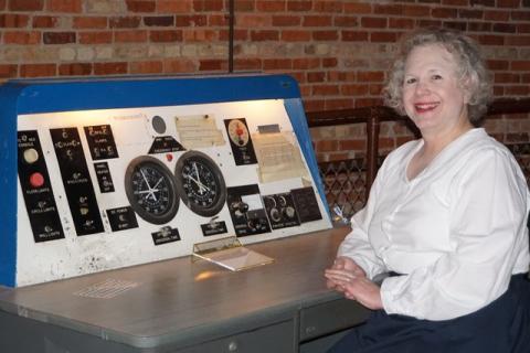 Presenter Rebecca Tulloch is in front of a vintage astronomy tool.  She is wearing a white Victorian style shirt with her white hair above her shoulders