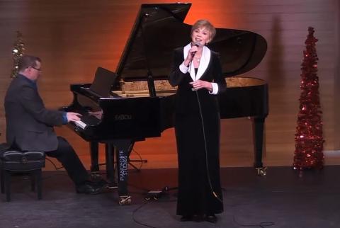 Pianist sits a black grand piano playing while singer is standing in a long black dress with white collar 