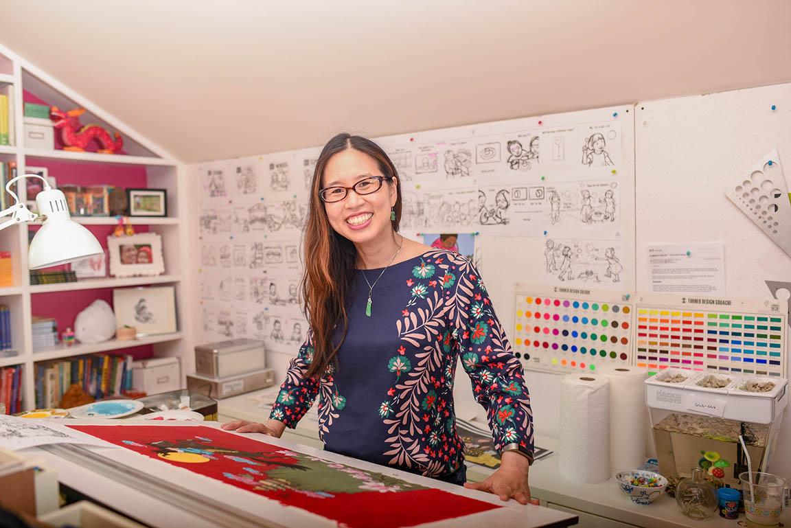 Photo of Grace Lin standing at her desk in her author studio