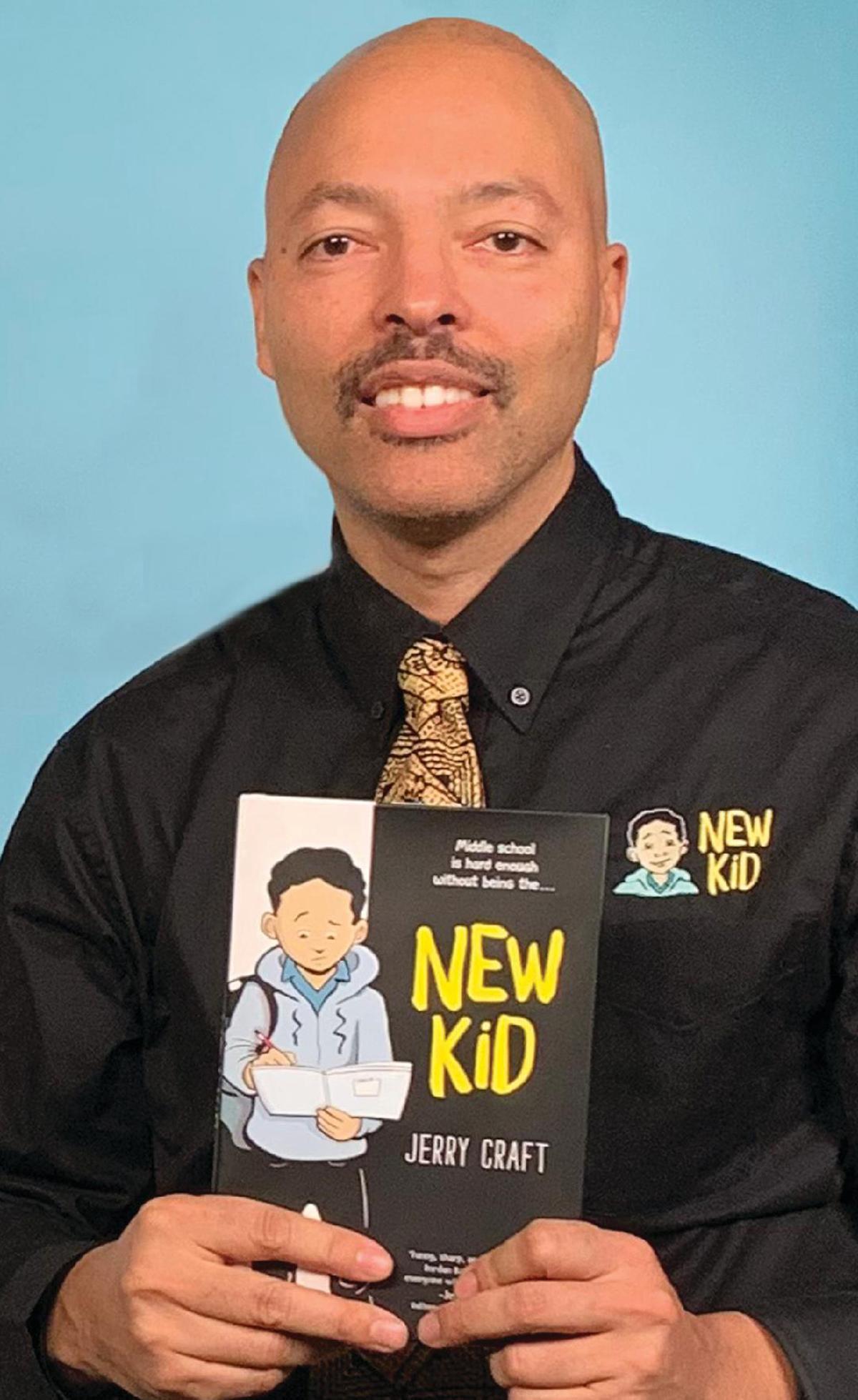 Photo of Jerry Craft holding his book, titled "New Kid," cover facing outward.